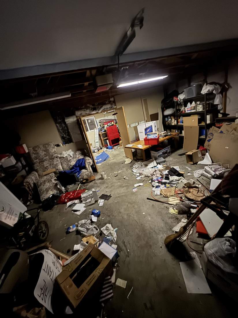 A cluttered garage packed with boxes, shelving, and old furniture before a cleanout